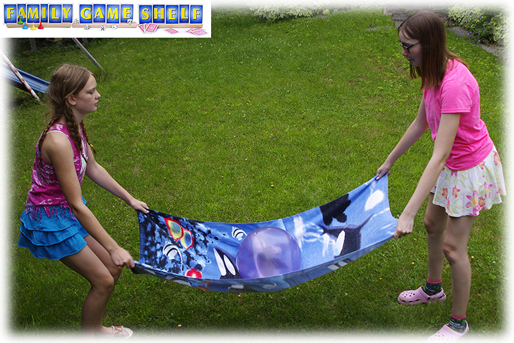 Two girls holding a colorful beach towel with a ball on it for this Luau Party game