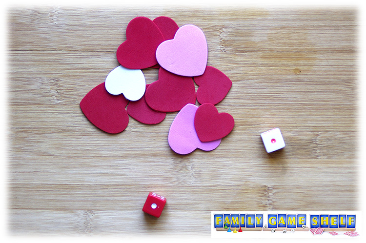 Two Valentine's Day Dice game Love is all around players with rolls of 1 and a pile of foam hearts in the middle