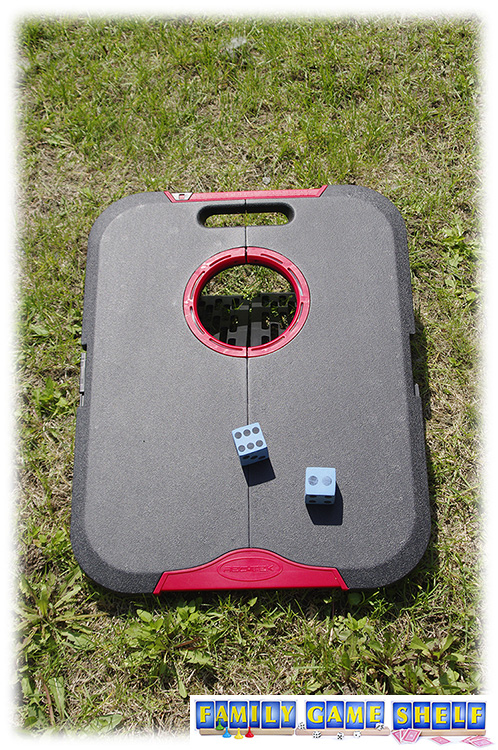 A cornhole board with two foam dice on it.