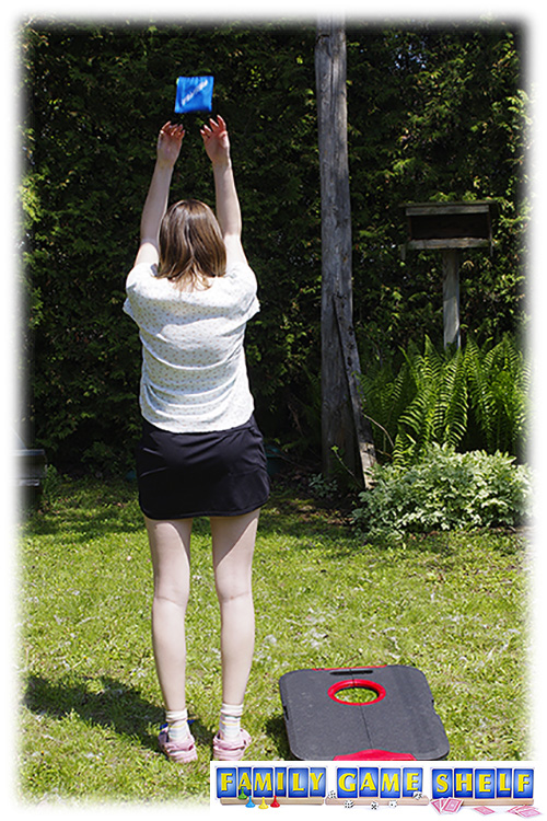 A woman playing Cornhole Golf throwing her beanbag while standing backwards 