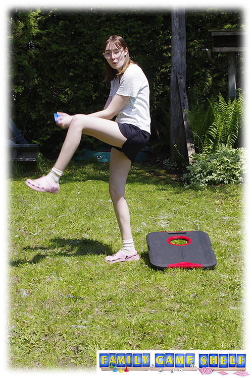 A woman playing cornhole golf throwing a beanbag like a baseball pitcher. 