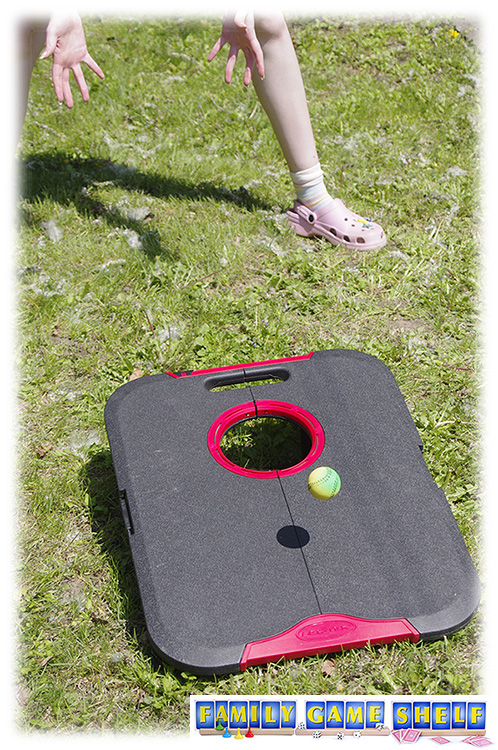 A woman playing Cornhole Lawn-Die variation trying to catch a bouncing ball after it hits the board