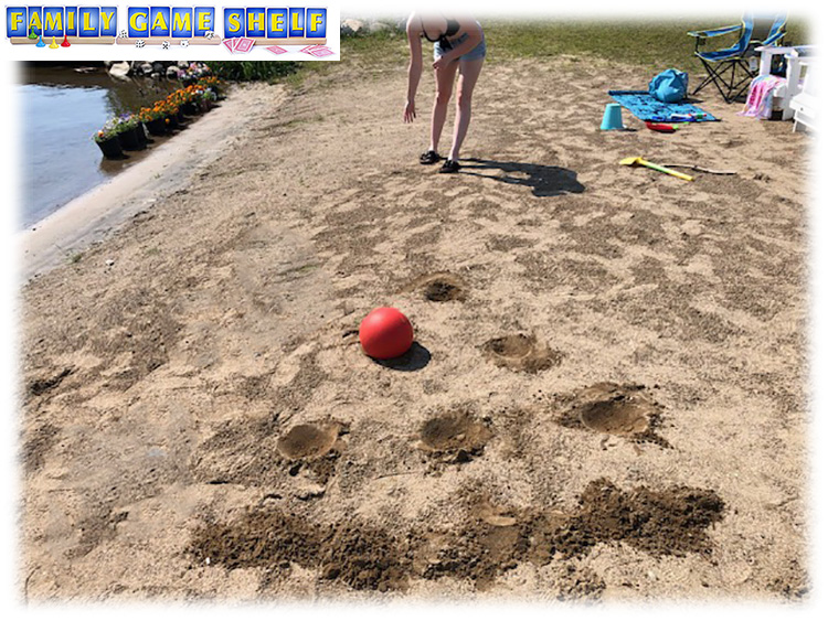 holes in the sand with a girl rolling a ball towards them