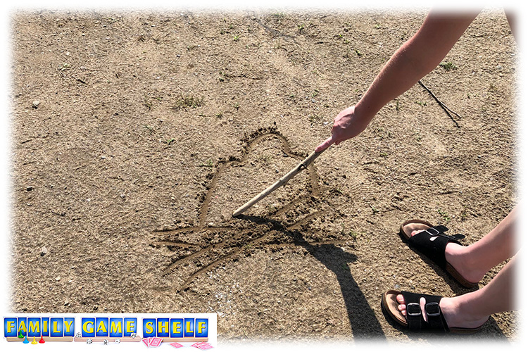 A girl drawing a camp fire in the sand with a stick